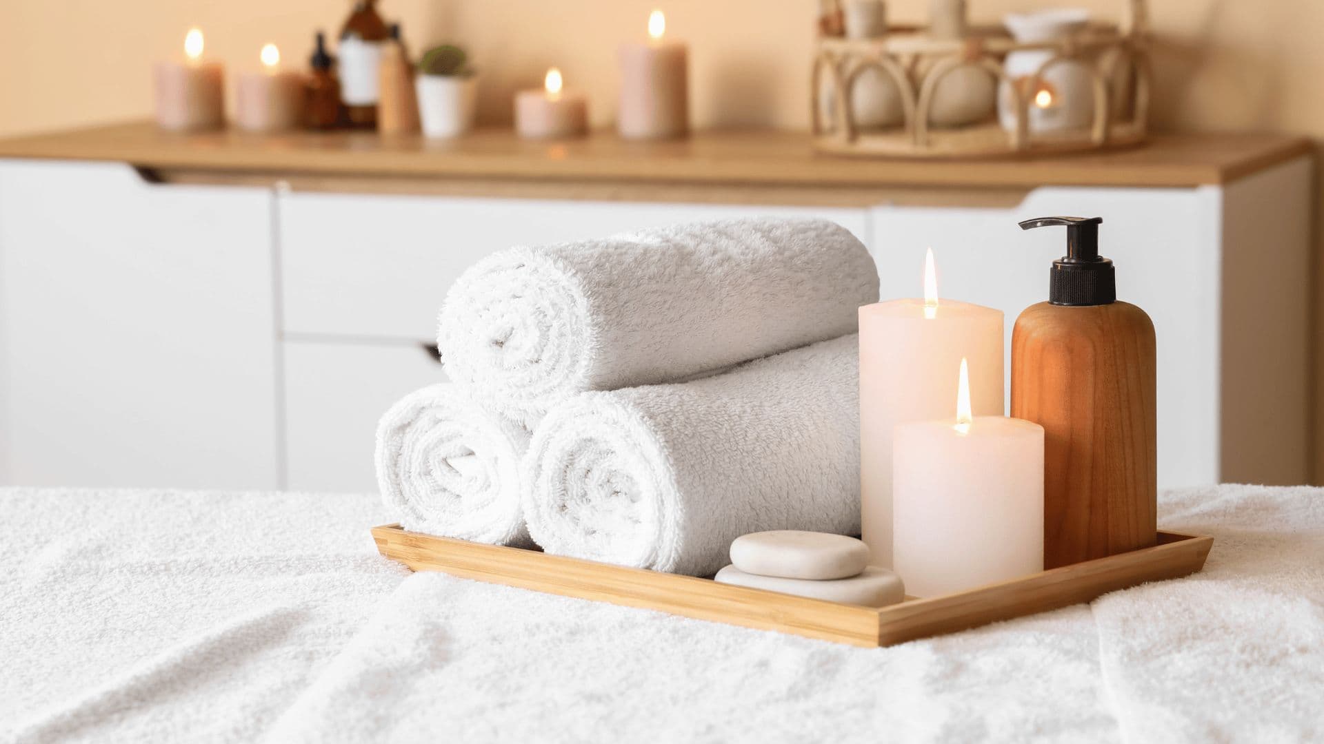Rolled towels, candles and a wooden dispenser on a spa table