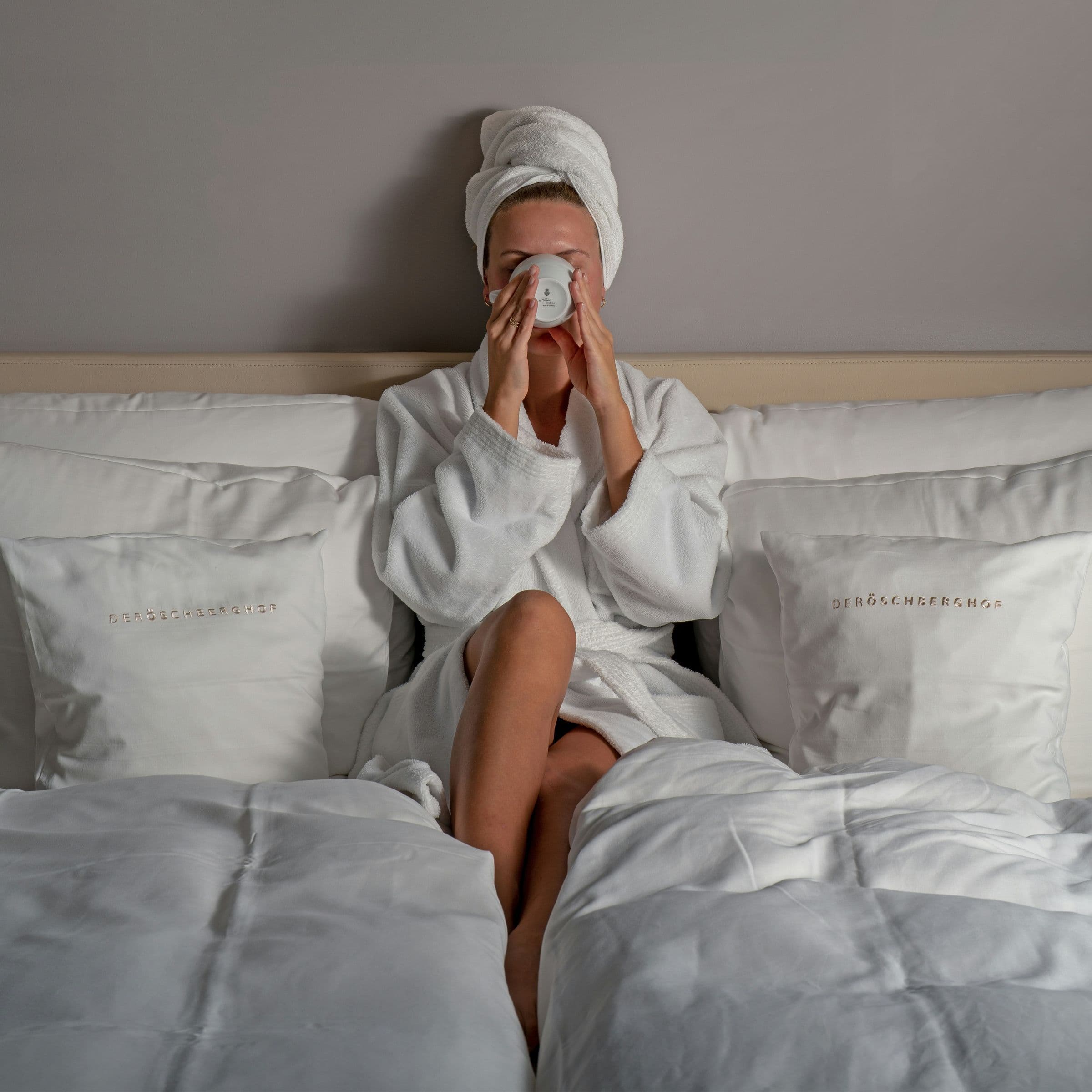 Guest in a white robe relaxing in a hotel bed