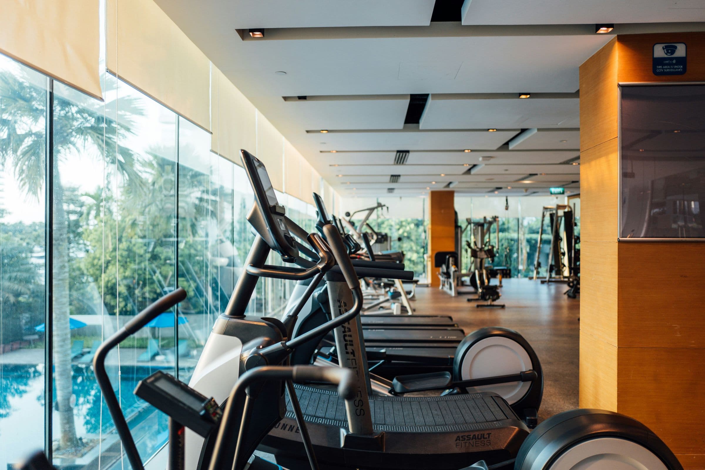 Cardio machines beside a glass-walled pool